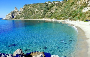 A coastal beach with clear blue water, rocky shore, and a hillside with vegetation. - Lovely apartment in Ricadi with WiFi (Ricadi)