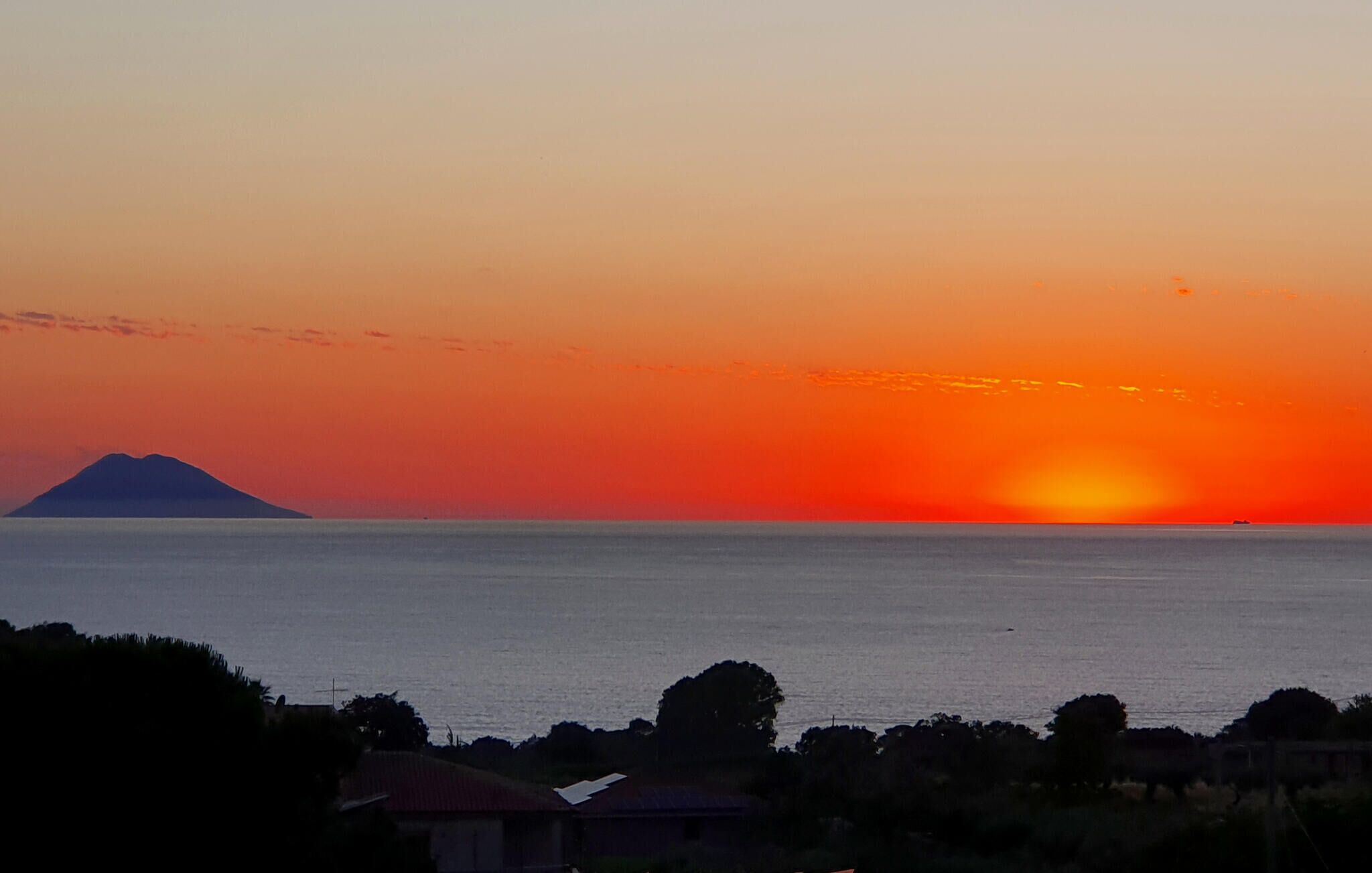 Ein Sonnenuntergang über einem Gewässer, im Hintergrund ein Berg.