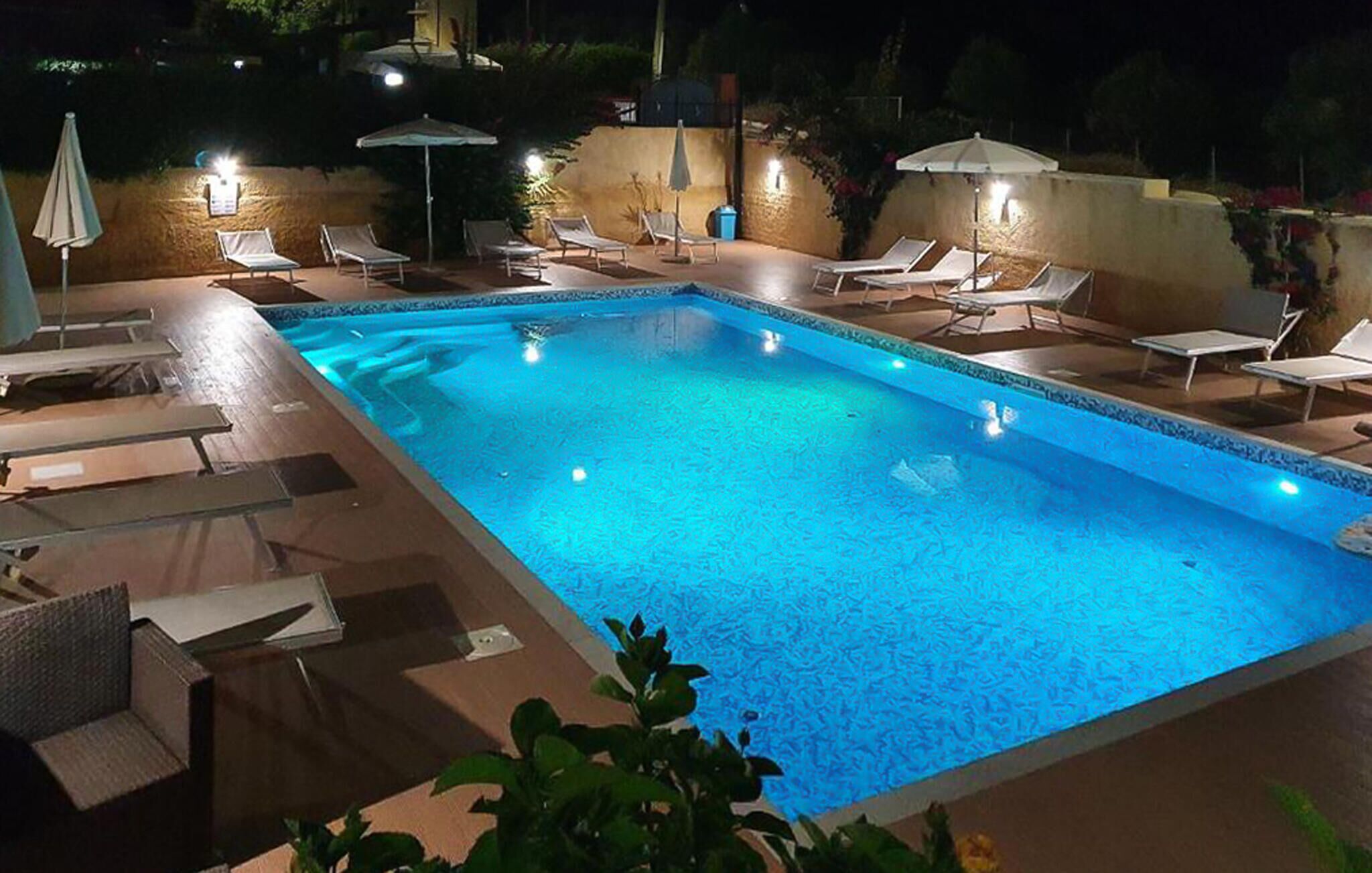 A rectangular swimming pool with a blue tint, surrounded by lounge chairs and umbrellas.