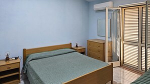 Un dormitorio con cama, mesita de noche, cómoda, armario y ventana con persianas.