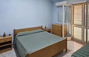 Ein Schlafzimmer mit Bett, Nachttisch, Schminktisch, Kleiderschrank und einem Fenster mit Jalousien.