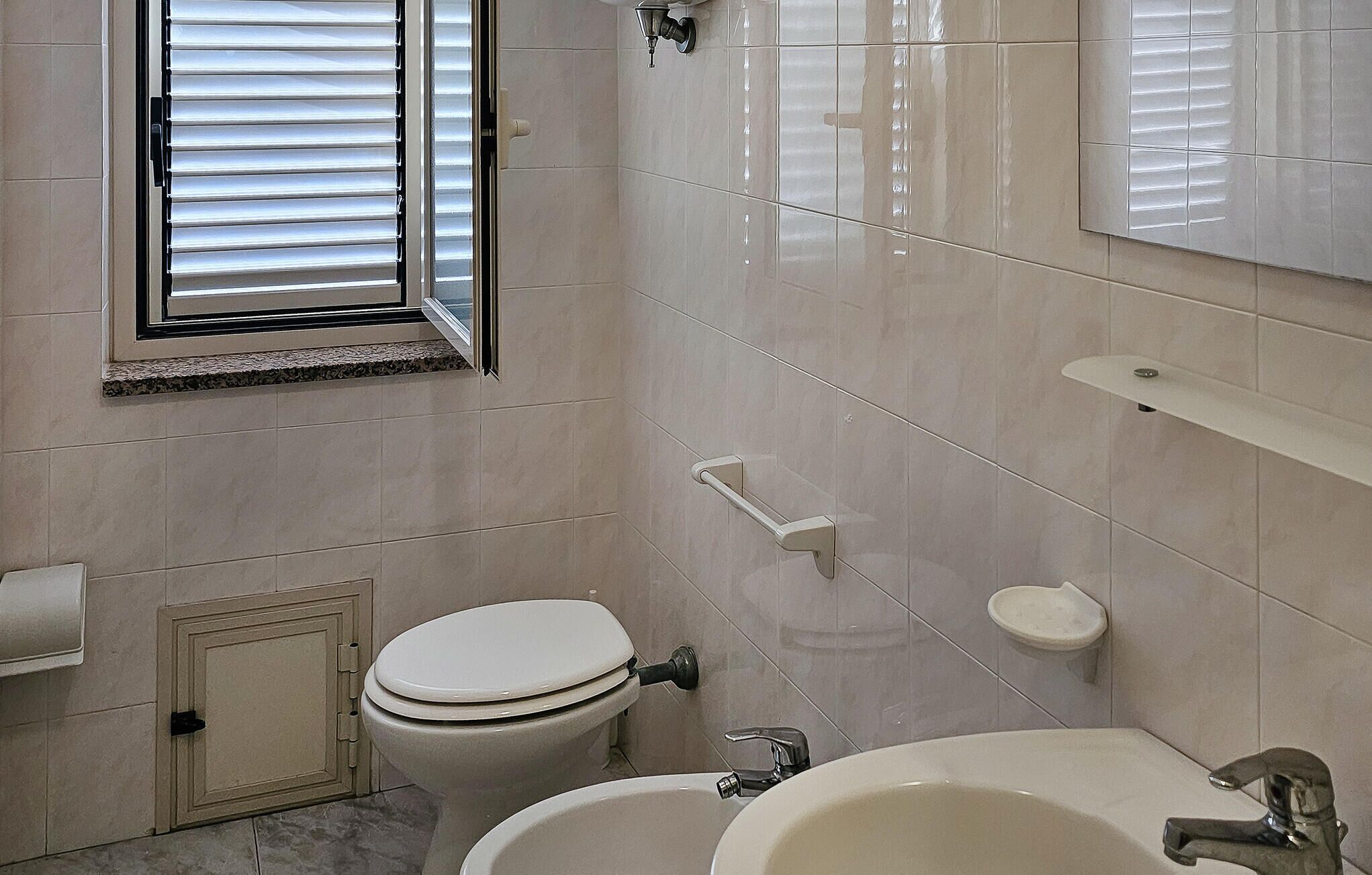 Een badkamer met toilet, wastafel en raam met zonwering.