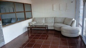 Una sala de estar con un sofá modular, una mesa de centro de vidrio y un ventanal con persianas.