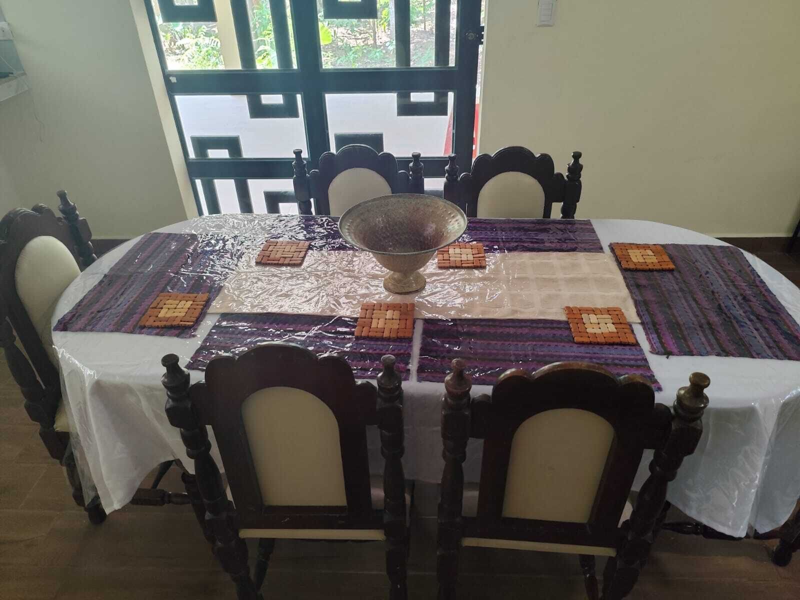 A round dining table with a white tablecloth, a central glass bowl, and patterned placemats.