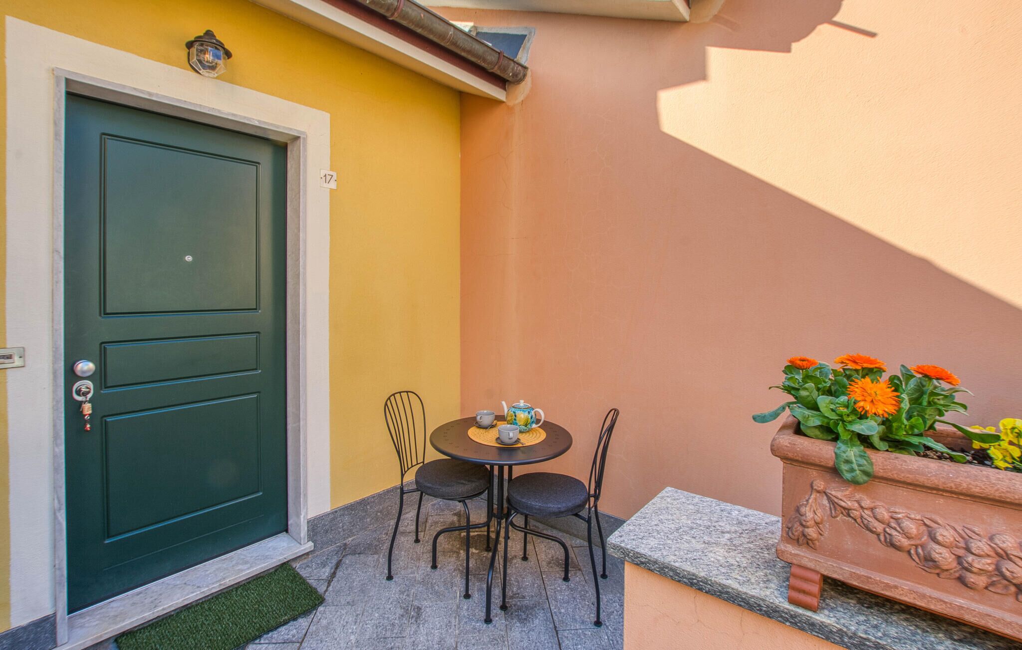 A green door, a small round table with chairs, and a potted plant with orange flowers.
