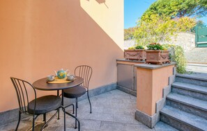 Ein kleiner Sitzbereich im Freien mit Tisch und Stühlen, einem Teekessel und zwei Tassen.