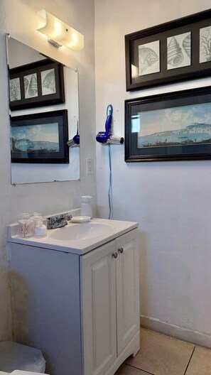 Une salle de bain avec un lavabo blanc, un miroir et des armoires, ainsi que deux œuvres d’art encadrées accrochées au mur.