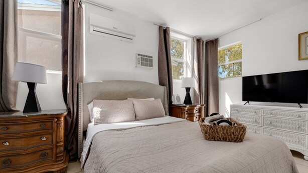 Une chambre à coucher avec un lit, une commode, une télévision et une fenêtre avec des rideaux.