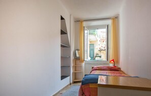 Une petite chambre avec un lit, une fenêtre, un bureau en bois et une échelle.