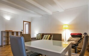 Un salon comprenant une table avec un plateau en verre, un canapé avec des coussins, un fauteuil, une lampe et une bibliothèque.