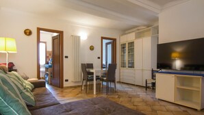 A living room with a sofa, a dining area with a table and chairs, a kitchen with cabinets and a TV.