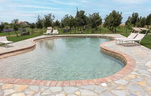 Une piscine à bord incurvé, entourée d’une terrasse en pierre et dotée de chaises longues.