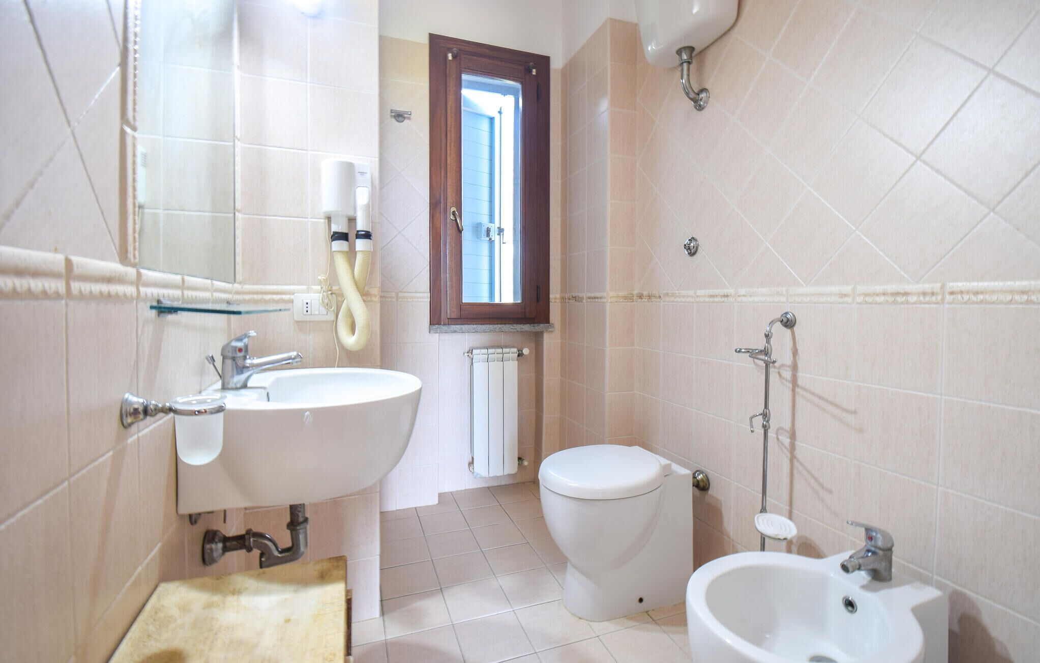 A bathroom with a sink, toilet, bidet, and a window.