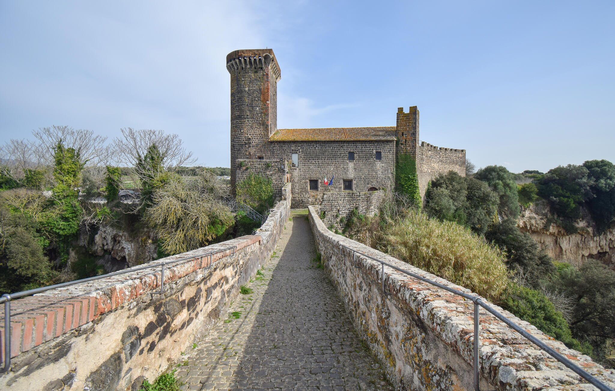 A stone pathway leading to a historic building with a tower, surrounded by greenery and a clear sky.