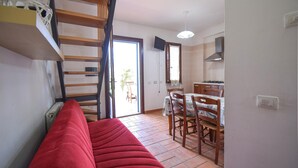 Ein Zimmer mit einem roten Sofa, einer Holztreppe, einem Essbereich mit Stühlen und einem Tisch sowie einer Küche mit einem Herd.
