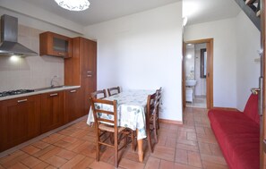 Una cocina compacta con armarios de madera, una mesa de comedor y sillas. Se ve un sofá rojo en la zona de estar contigua.