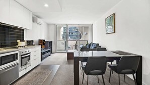 Eine moderne Küche mit integrierten Geräten, ein Essbereich mit einem Glastisch und Blick auf eine Stadtlandschaft durch große Fenster.