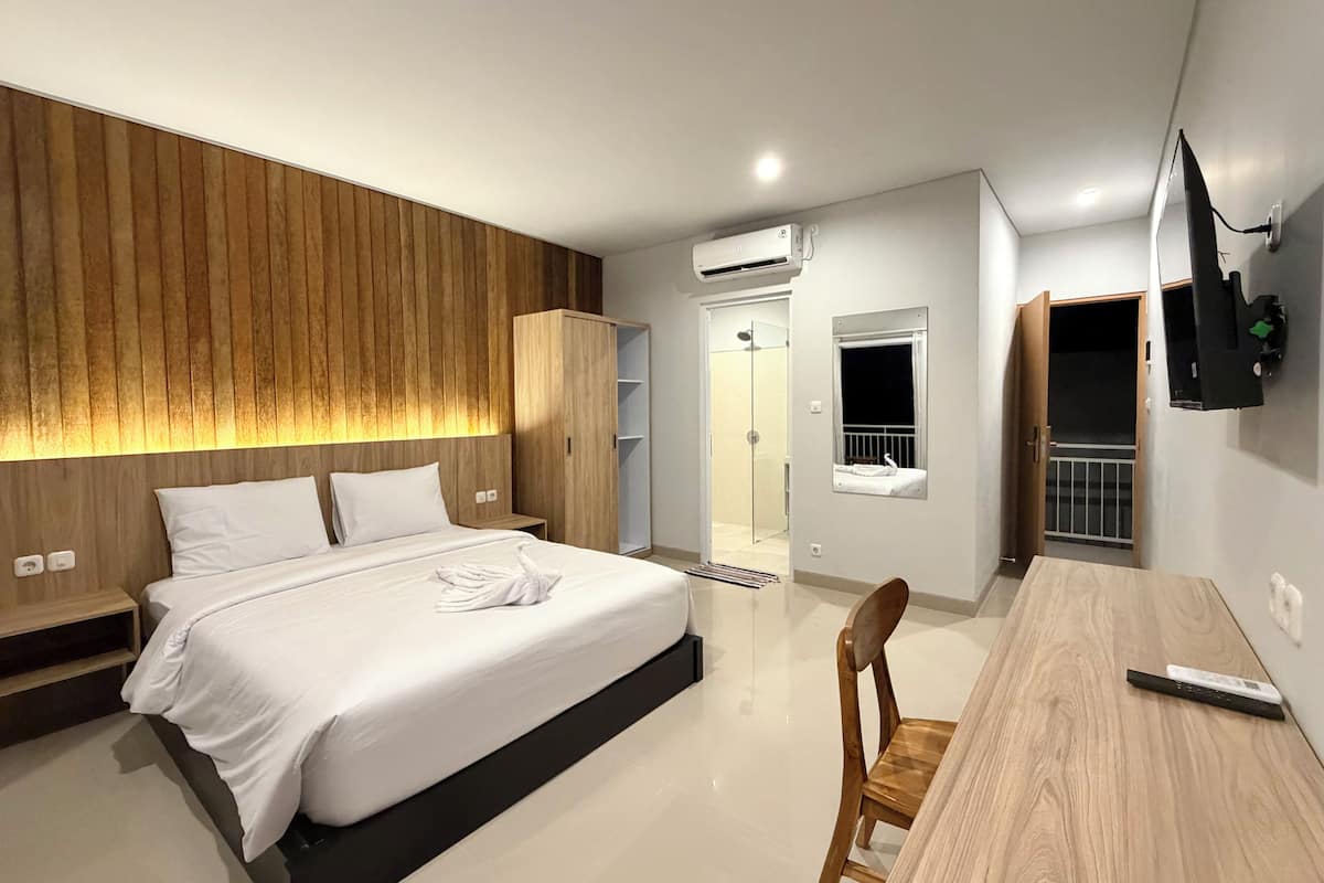 A modern hotel room with a bed, bedside table, wardrobe, and a TV mounted on the wall.