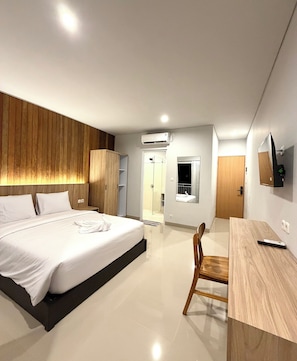 A modern hotel room with a large bed, a desk, a chair, an air conditioning unit, and a mirror on the wall. - Double A Cozy Living (Canggu)