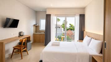 Habitación de hotel con cama, escritorio, silla, televisor, kitchenette y balcón con vistas.