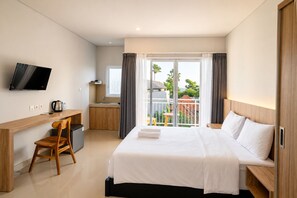 A hotel room with a bed, a desk, a chair, a television, a kitchenette, and a balcony with a view. - Double A Cozy Living (Tumbak Bayuh)