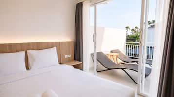 Habitación de hotel con una cama grande, una mesita, dos sillas y un balcón con vista a palmeras.