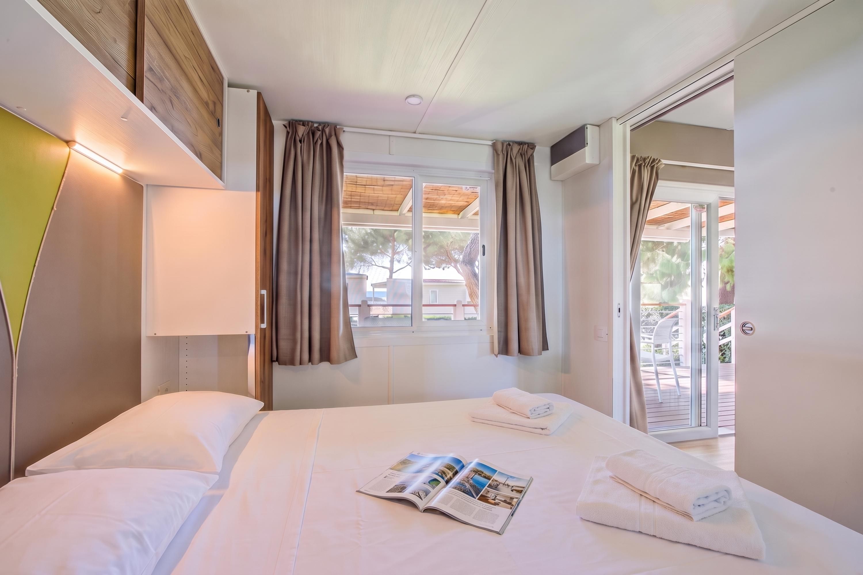 Ein Hotelzimmer mit einem Bett, einem Vorhangfenster, einer Tür zu einem Außenbereich und einer Zeitschrift auf dem Bett.