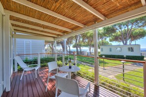 A covered outdoor area with a wooden ceiling, white chairs, a table with a bottle and glass, and a view of the sea and trees. - Sea View - 40 Parallelo - Deluxe 25, Marina di Camerota, Italy (Marina di Camerota)