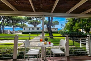 A covered outdoor seating area with two chairs and a table, overlooking a well-maintained lawn and a distant building. - Sea View - 40 Parallelo - Deluxe 25, Marina di Camerota, Italy (Marina di Camerota)