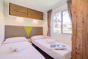 Een hotelkamer met twee bedden, een houten hoofdbord, een raam met gordijnen en een tijdschrift op het bed.