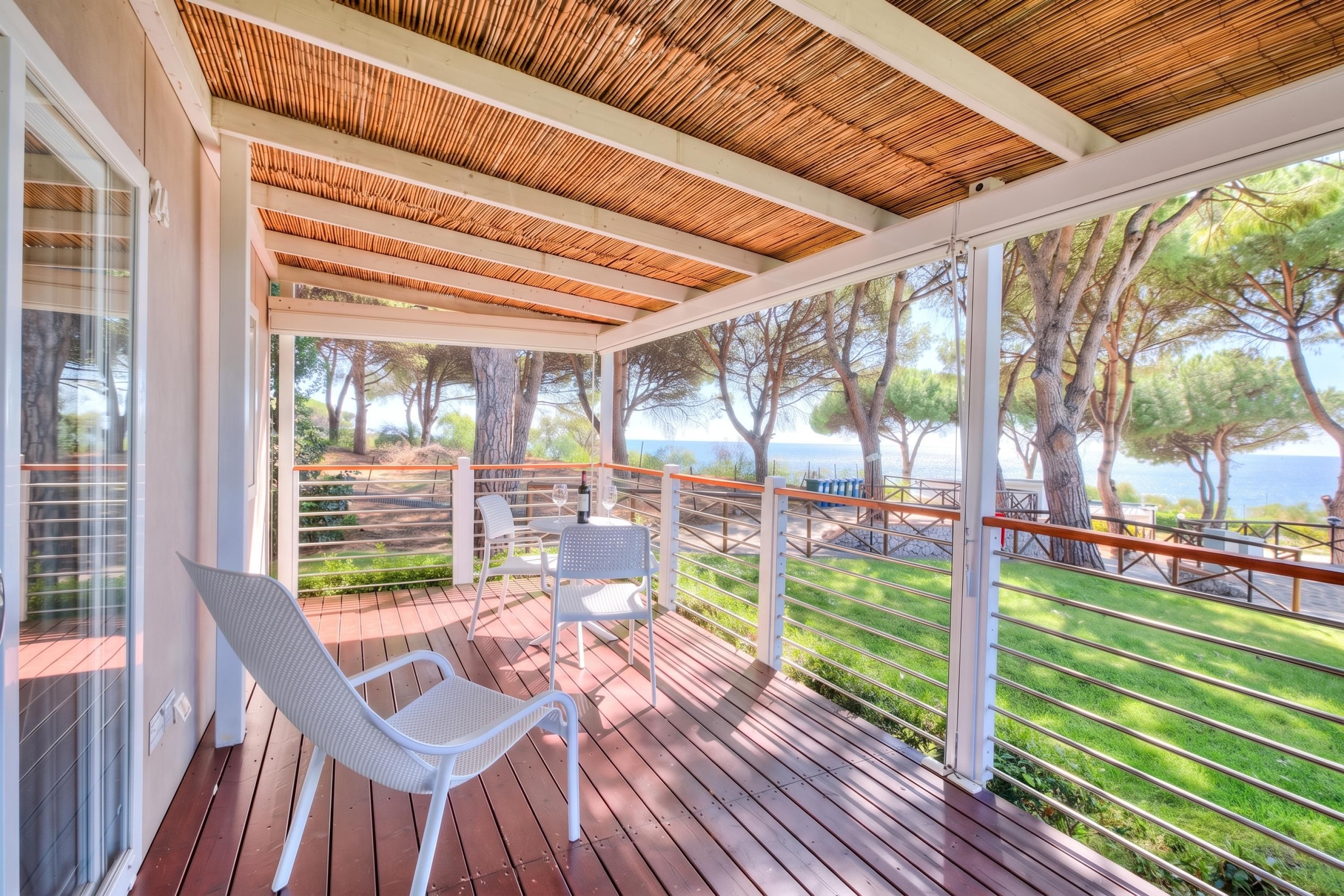 A covered outdoor area with a wooden deck, white chairs, and a view of the sea.