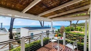 Eine überdachte Terrasse im Freien mit Blick auf das Meer, ein Tisch mit Stühlen und ein Blumentopf.