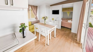 Een moderne, goed verlichte kamer met een eettafel, stoelen, een televisie en een bank.