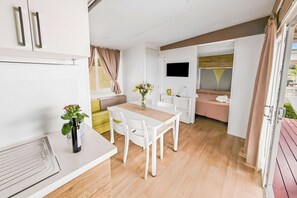 Een moderne, goed verlichte kamer met een eettafel, stoelen, een televisie en een bank.