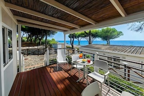 A covered outdoor area with a wooden deck, white chairs, a table with a drink, and a view of the sea and trees. - Sea View - 40 Parallelo - Deluxe 22, Marina di Camerota, Italy (Marina di Camerota)