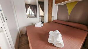 Een net opgemaakt bed met witte handdoeken, een houten hoofdbord en een raam met gordijnen.