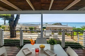 Una mesa con una bebida, un cuenco de fruta y una planta en maceta en un balcón con vistas a la costa.