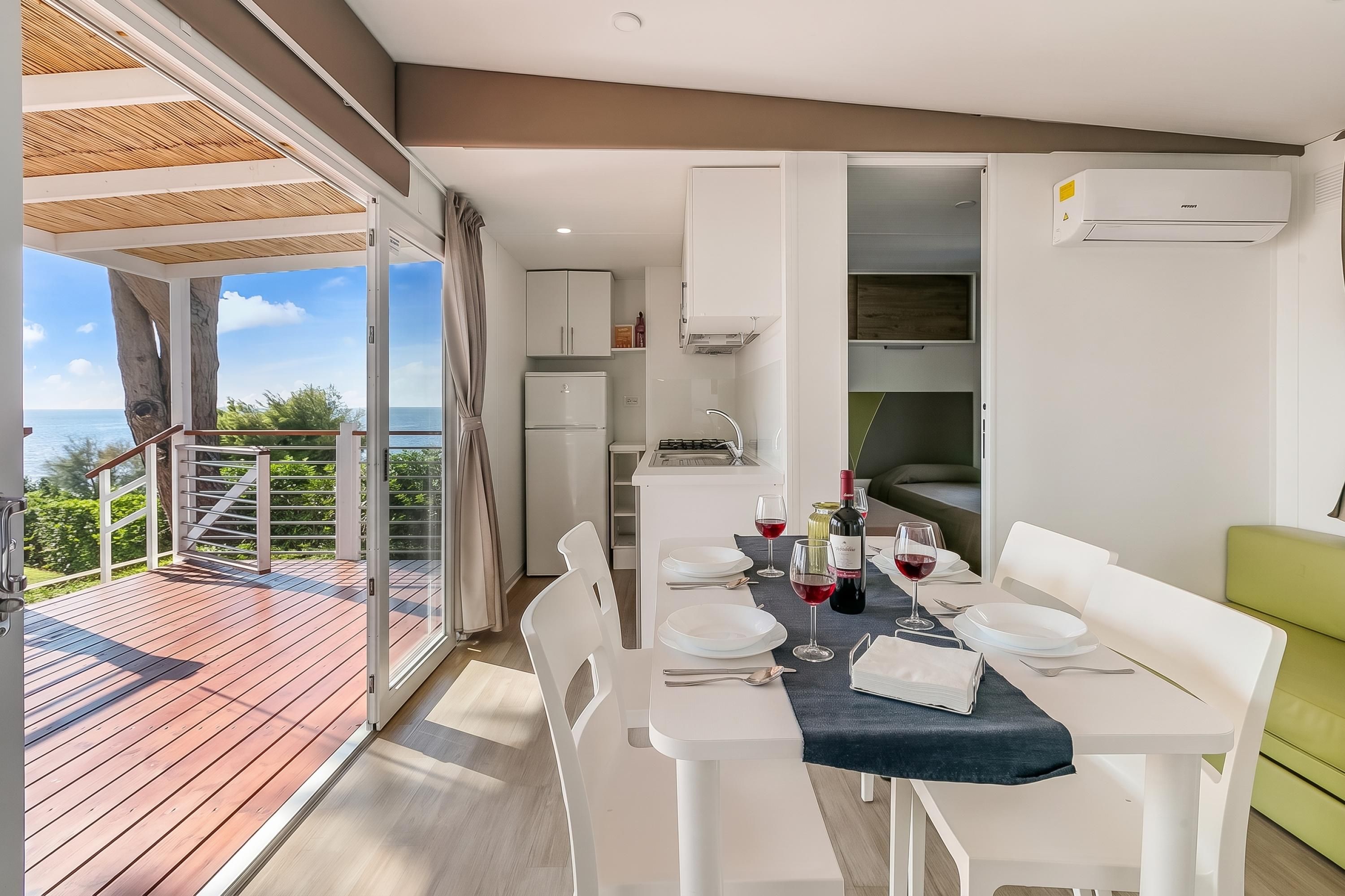 A dining area with a table set for two, a view of the sea, and a balcony with a wooden deck.