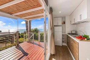 Eine moderne Küche mit Meerblick, ein Balkon mit Holzboden und eine Glastür, die man aufschieben kann.