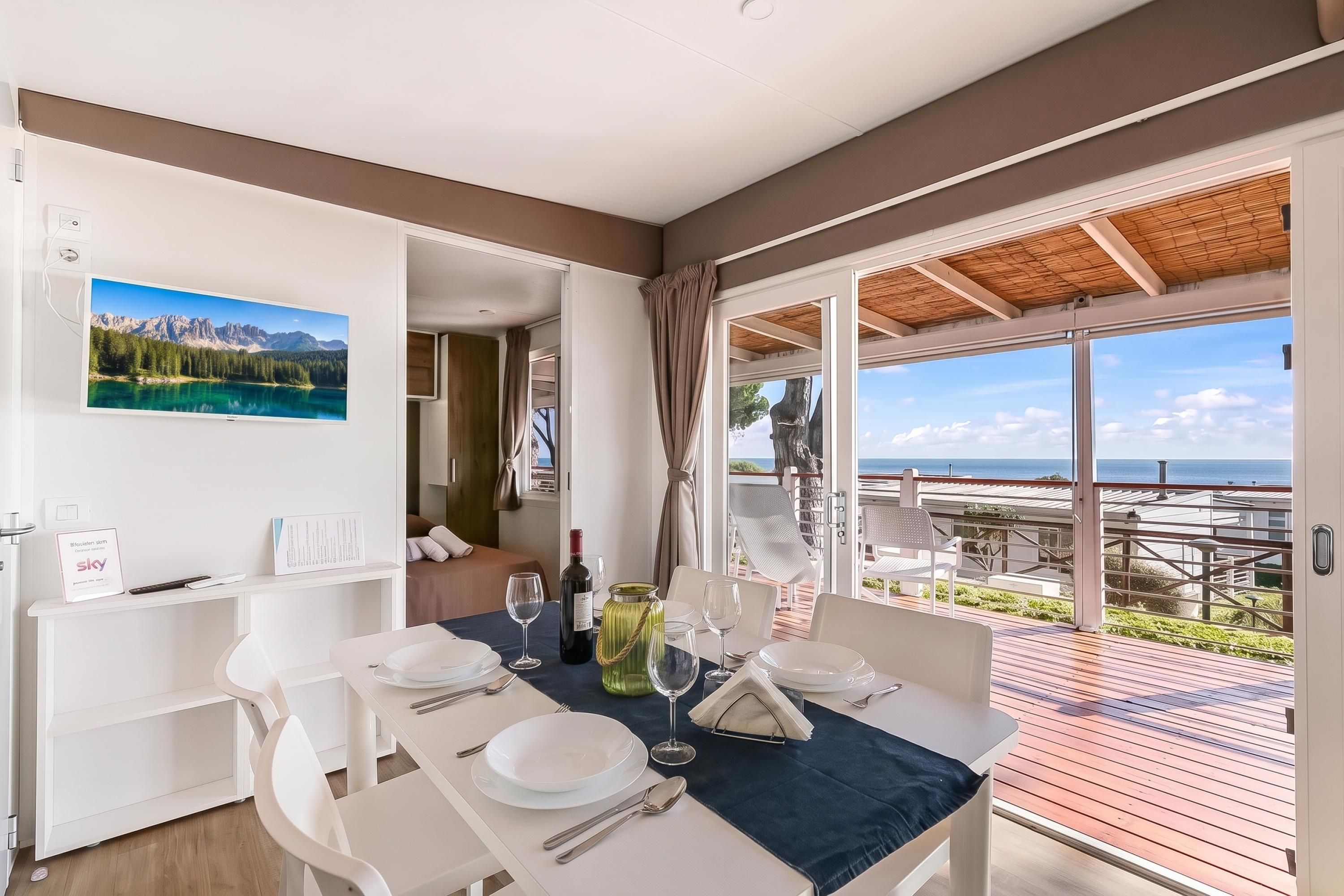 A dining area with a table set for two, a view of the sea, and a mountain landscape on the wall.