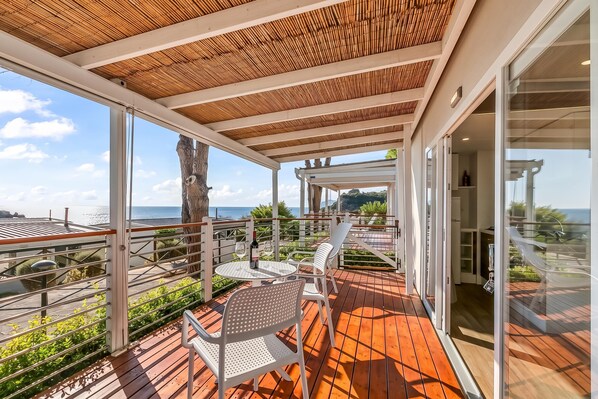 A covered outdoor area with a wooden ceiling, a table with chairs, and a view of the sea.