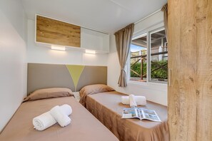 A hotel room with two beds, a window with curtains, a wooden headboard, and a magazine on the windowsill.