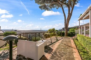 Una terraza en la azotea con vistas al mar, un pérgola y un área de estar exterior blanca.