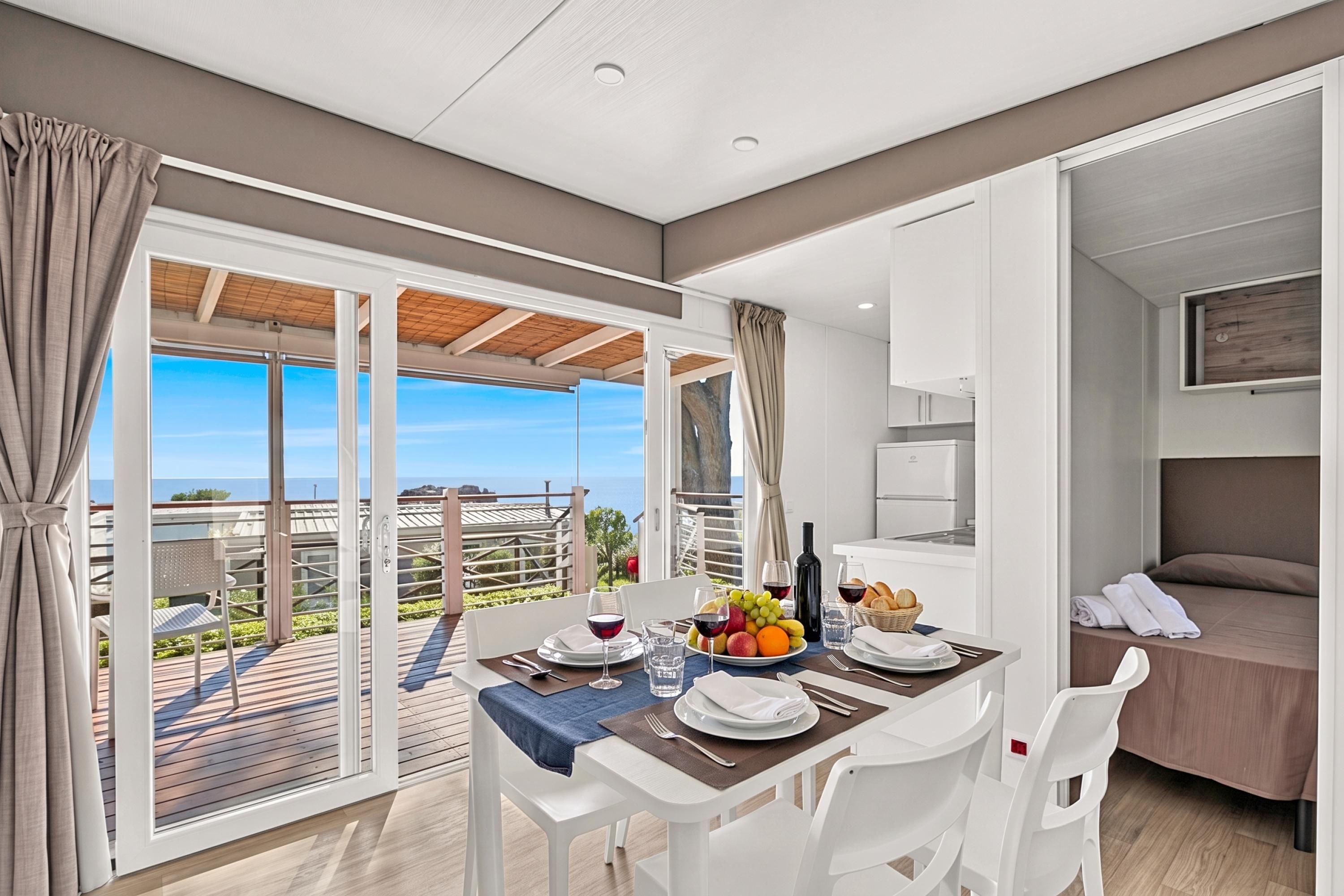 Une chambre d’hôtel moderne avec balcon, un coin repas avec une table dressée pour deux personnes et un lit.