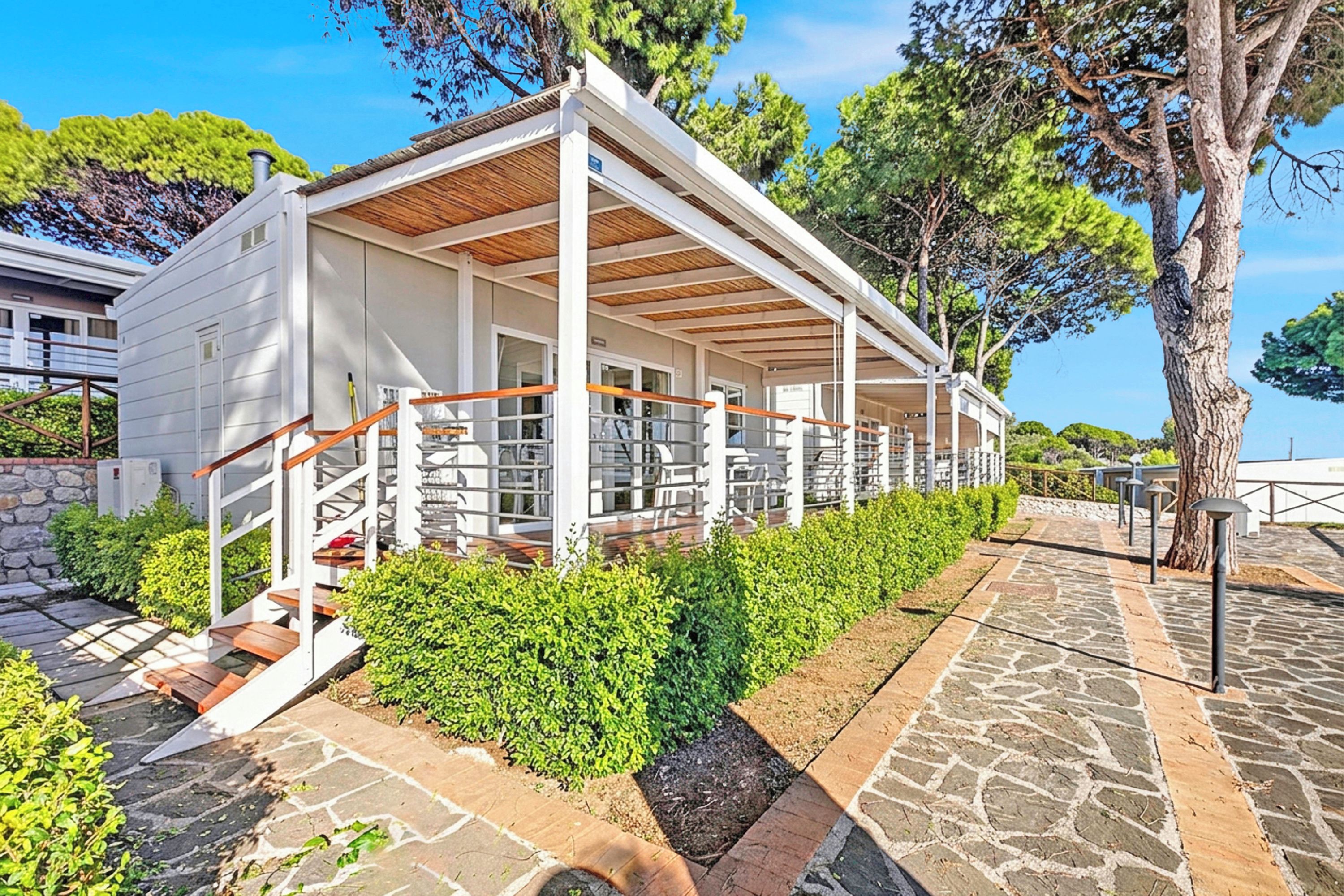 A modern building with a covered patio area, stone pathway, and lush greenery.