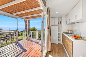 A modern kitchen with a view of the sea, a wooden deck, and a balcony with a railing.