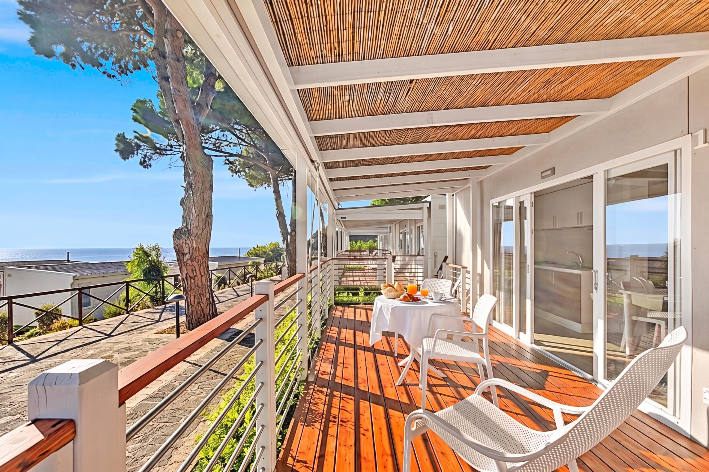 Een balkon met een houten terras, witte meubels en uitzicht op zee.