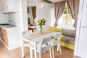 Une cuisine compacte équipée d’une cuisinière à gaz, d’un évier et de meubles blancs. On y trouve un coin repas avec une table et des chaises, ainsi qu’un canapé agrémenté de rideaux.