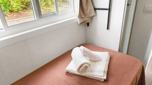 A small, single-bed room with a window, a towel on the bed, and a coat hanging on a rack.