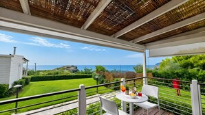 Un balcón con mesa y sillas, con vistas a un paisaje verde y el mar.